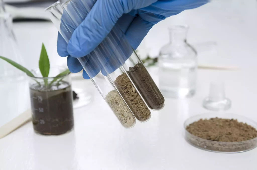 Gloved hand holds three test tubes with different soil samples in a lab, with a